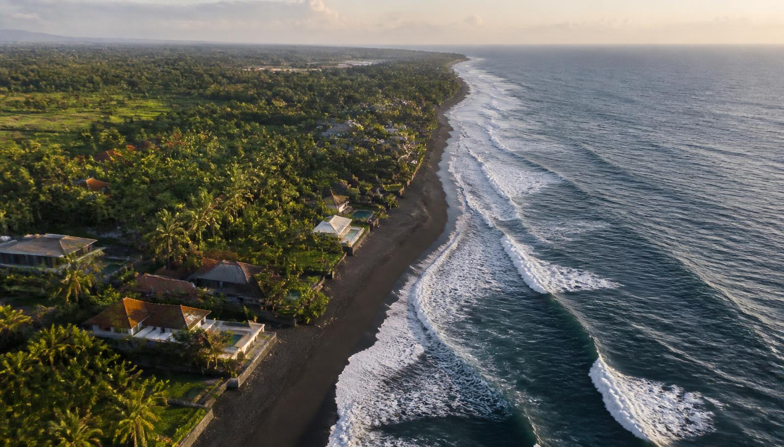 Luchtfoto van de kust van Bali met zwart strand, palmen en villa's tussen het groen