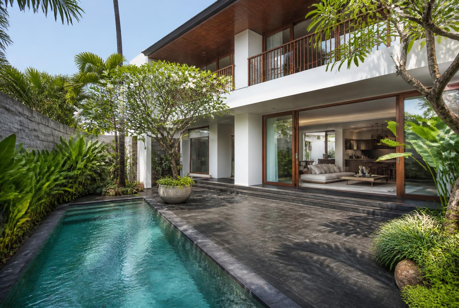 Tweelaagse villa in Canggu met wit stucwerk, houten details, lange pool en tropische tuin